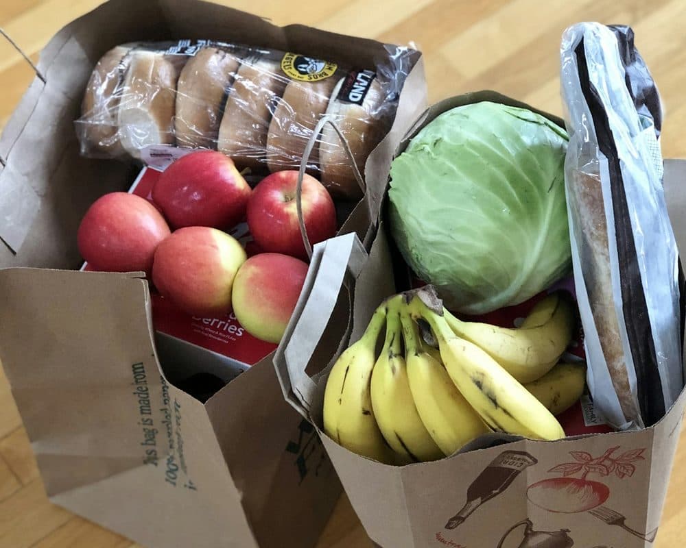 Two paper grocery bags packed with apples, bananas, a cabbage, bread and rolls